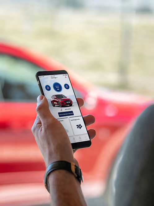 A person using a Ford mobile application to remotely control a red SUV vehicle visible blurred in the background.