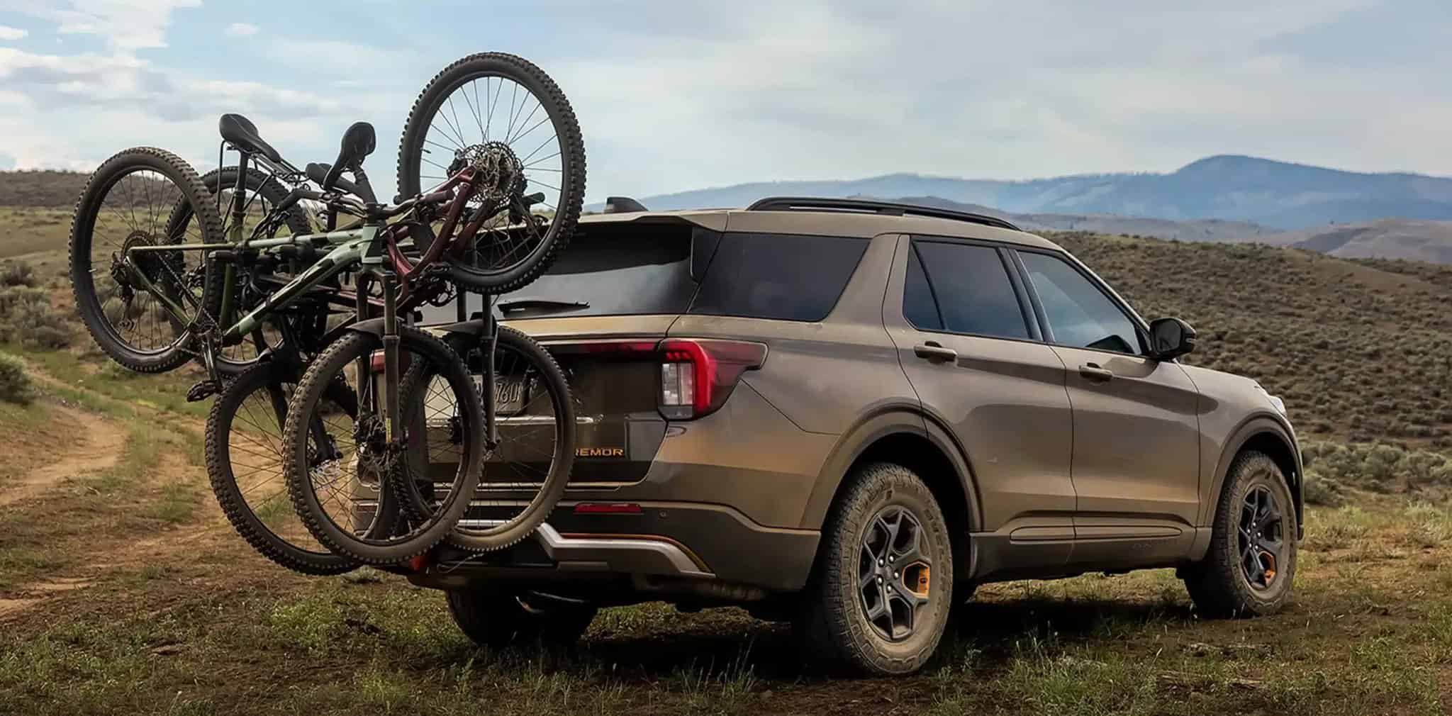 2027 Ford Explorer rear three-quarter view with bikes on a rack, grassy hills